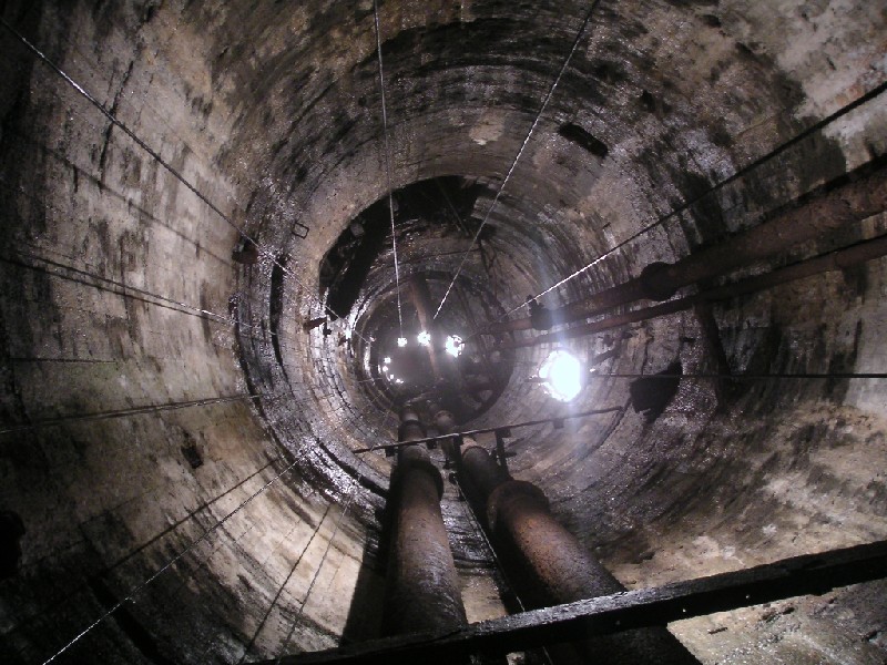bs_lookingdown_selflit_8.jpg - Looking down the Brewery Shaft with the lights all the way down to the bottom, a total of 100m (328'). The dark alcove is were a compressed air winch is housed and the pipe across the shaft is the Rampgill Horse Level.