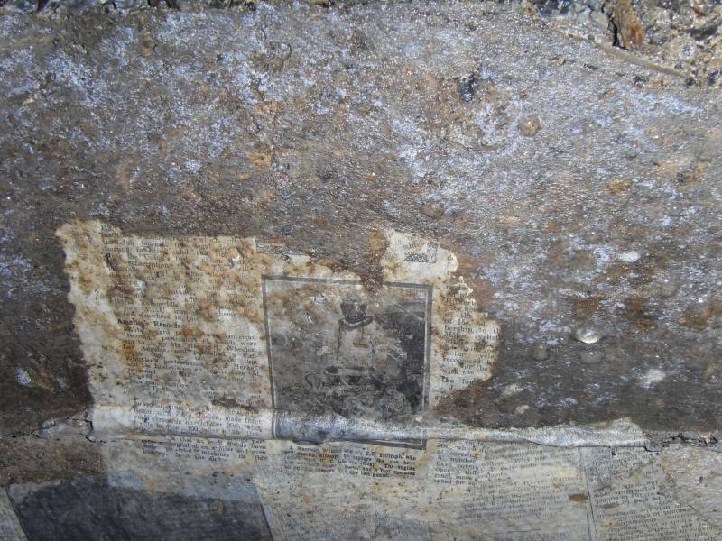 41_parallelv_archnewsp3.jpg - Newspapers on concrete arching, preserved by a thin layer of calcite. This is not a picture of a space man, but rather "J. Harrison Watson and his T.T. Triumph, who will shortly attempt to capture the one hour...."