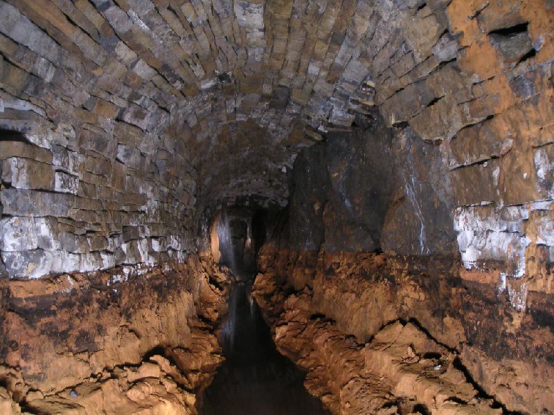 brownleyh_gbxvein_mud1.jpg - After the collapses we came to stone arched passage. From here to the Guddamgill Horse Level junction the floor was covered in this orange sticky mud. In the background there is a fall of water coming from an ore hopper.